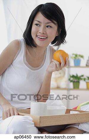 Young woman having breakfast in bed, holding orange, looking away View Large Photo Image Stock Image - Young woman having breakfast in bed, holding orange, looking away. Fotosearch