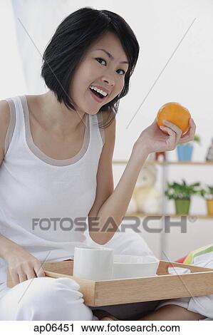 Young woman having breakfast in bed, holding orange, smiling View Large Photo Image Stock Image - Young woman having breakfast in bed, holding orange, smiling. Fotosearch