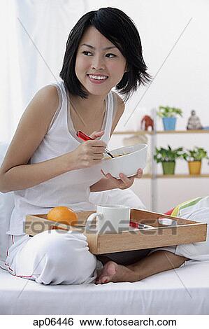 Stock Photograph - Young woman having breakfast in bed. Fotosearch