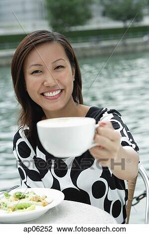 Young woman holding cappuccino cup, towards camera View Large Photo Image Stock Image - Young woman holding cappuccino cup, towards camera. Fotosearch