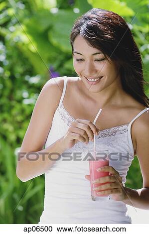 Stock Image - Young woman holding drink, smiling, looking away. Fotosearch
