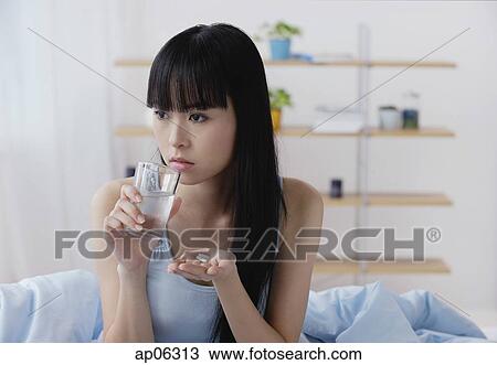 Young woman holding glass of water and pills, looking away View Large Photo Image Stock Image - Young woman holding glass of water and pills, looking away. Fotosearch