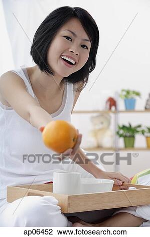 Young woman holding orange towards camera, smiling View Large Photo Image Stock Image - Young woman holding orange towards camera, smiling. Fotosearch