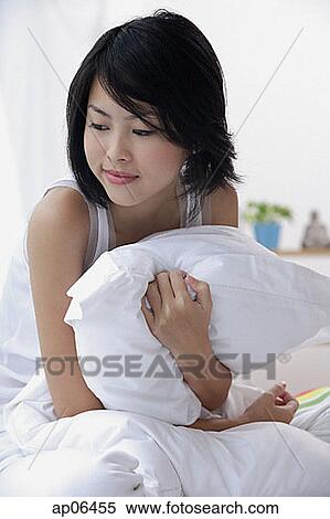 Stock Photography - Young woman hugging pillow, looking away. Fotosearch