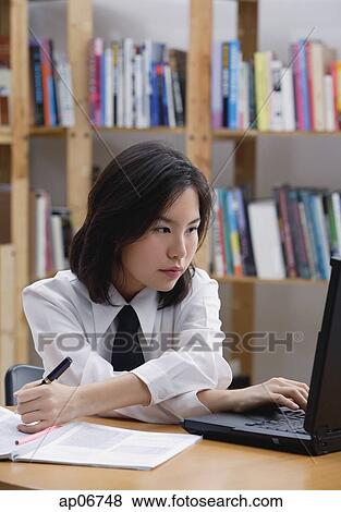 Young woman in library, using laptop and writing View Large Photo Image Stock Photo - Young woman in library, using laptop and writing. Fotosearch