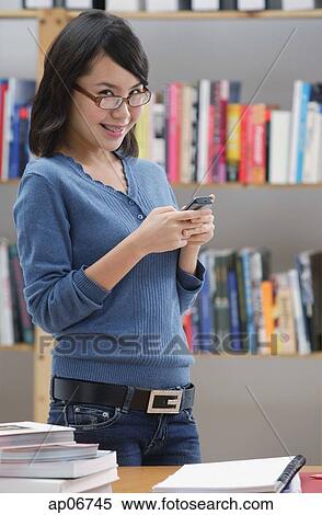 Young woman in library, using mobile phone, looking at camera View Large Photo Image Stock Photography - Young woman in library, using mobile phone, looking at camera. Fotosearch