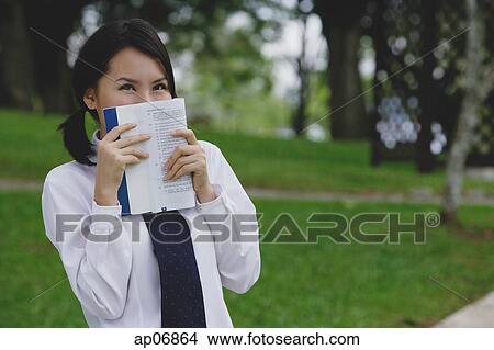 Picture - Young woman in school uniform, book covering face. Fotosearch