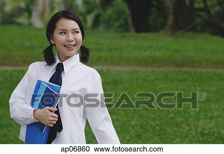 Stock Image - Young woman in school uniform, standing in park, looking away. Fotosearch