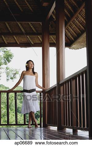 Stock Photo - Young woman in white dress standing in balcony, looking away. Fotosearch