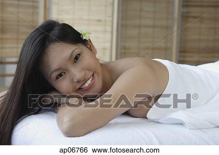 Young woman lying down on massage table, smiling at camera View Large Photo Image Stock Photograph - Young woman lying down on massage table, smiling at camera. Fotosearch