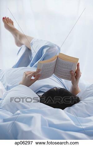 Young woman lying in bed, reading a book View Large Photo Image Stock Photo - Young woman lying in bed, reading a book. Fotosearch