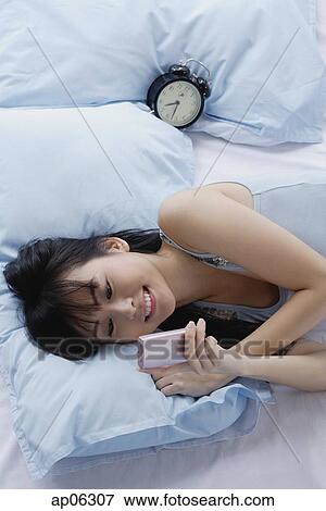 Young woman lying on bed, looking at mobile phone View Large Photo Image Stock Photo - Young woman lying on bed, looking at mobile phone. Fotosearch