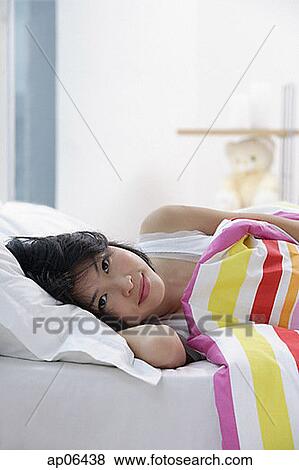 Young woman lying on bed, looking at camera View Large Photo Image Stock Photo - Young woman lying on bed, looking at camera. Fotosearch