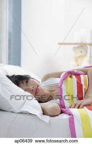 Young woman lying on bed, looking away View Large Photo Image Stock Photo - Young woman lying on bed, looking away. Fotosearch