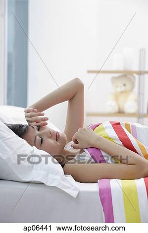 Young woman lying on bed, rubbing her eyes View Large Photo Image Stock Image - Young woman lying on bed, rubbing her eyes. Fotosearch