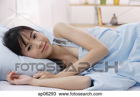 Stock Image - Young woman lying on bed, smiling. Fotosearch