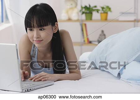 Young woman lying on bed, using laptop View Large Photo Image Stock Image - Young woman lying on bed, using laptop. Fotosearch