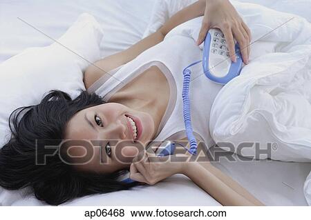 Young woman lying on bed, using telephone, smiling at camera View Large Photo Image Stock Photo - Young woman lying on bed, using telephone, smiling at camera. Fotosearch