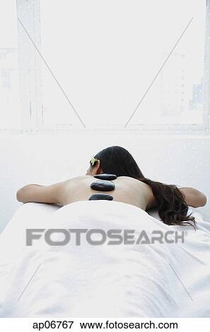 Young woman lying on massage table, massage stones along her back View Large Photo Image Stock Photo - Young woman lying on massage table, massage stones along her back. Fotosearch