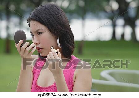 Young woman outdoors, looking at compact, applying make-up View Large Photo Image Picture - Young woman outdoors, looking at compact, applying make-up. Fotosearch