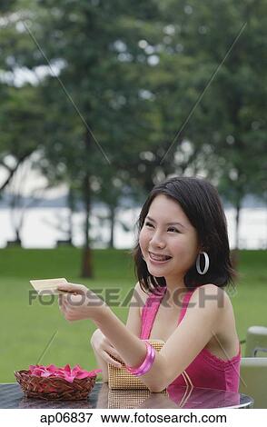 Stock Photo - Young woman sitting at outdoor table, paying with credit card. Fotosearch