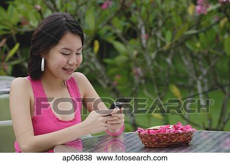 Young woman sitting at outdoor table, looking at mobile phone View Large Photo Image Stock Photo - Young woman sitting at outdoor table, looking at mobile phone. Fotosearch