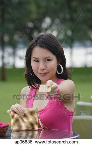 Stock Photograph - Young woman sitting at outdoor table, holding credit card towards camera. Fotosearch