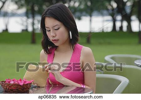 Stock Photography - Young woman sitting at outdoor table, looking into wallet. Fotosearch