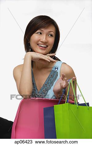 Young woman sitting, holding shopping bags, looking away View Large Photo Image Stock Image - Young woman sitting, holding shopping bags, looking away. Fotosearch