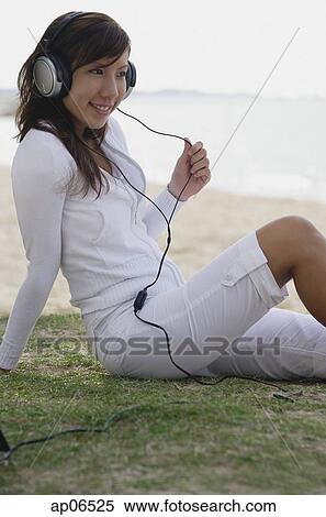 Young woman sitting on beach, listening to music, wearing headphones View Large Photo Image Stock Photography - Young woman sitting on beach, listening to music, wearing headphones. Fotosearch
