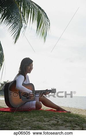 Young woman sitting on beach playing a guitar View Large Photo Image Stock Photography - Young woman sitting on beach playing a guitar. Fotosearch