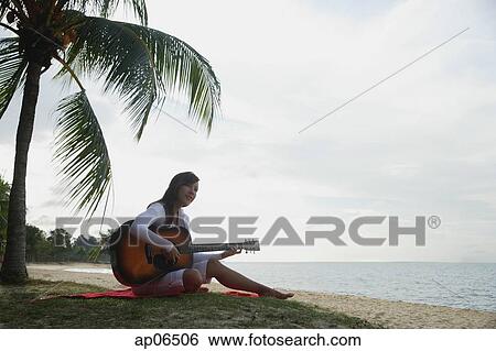 Young woman sitting on beach with a guitar View Large Photo Image Stock Photograph - Young woman sitting on beach with a guitar. Fotosearch