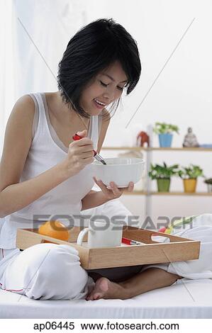Young woman sitting on bed, having breakfast View Large Photo Image Stock Photography - Young woman sitting on bed, having breakfast. Fotosearch