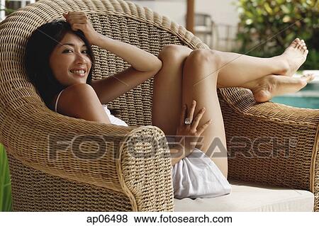 Young woman sitting on wicker chair, looking at camera View Large Photo Image Stock Photo - Young woman sitting on wicker chair, looking at camera. Fotosearch