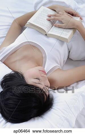 Picture - Young woman sleeping on bed, holding book. Fotosearch
