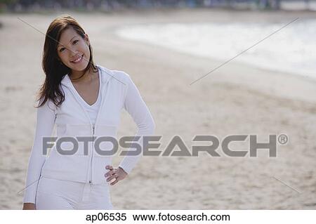 Young woman standing on beach, hand on hip, smiling at camera View Large Photo Image Stock Photography - Young woman standing on beach, hand on hip, smiling at camera. Fotosearch
