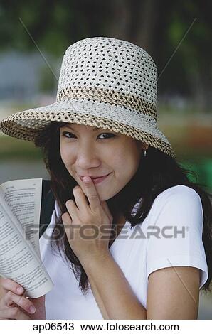 Young woman wearing hat, holding book, finger on mouth View Large Photo Image Stock Image - Young woman wearing hat, holding book, finger on mouth. Fotosearch