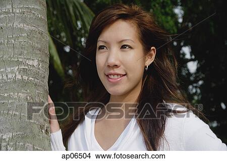 Young woman with hand on tree trunk, looking away View Large Photo Image Picture - Young woman with hand on tree trunk, looking away. Fotosearch