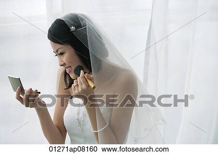 Stock Image - A bride does her makeup in the mirror. Fotosearch