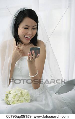 Stock Photo - A bride does her makeup in the mirror. Fotosearch