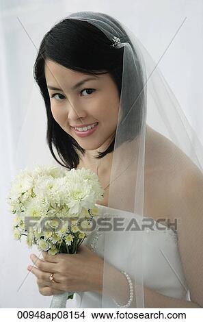 A bride with a bouquet of flowers looks at the camera View Large Photo Image Picture - A bride with a bouquet of flowers looks at the camera. Fotosearch