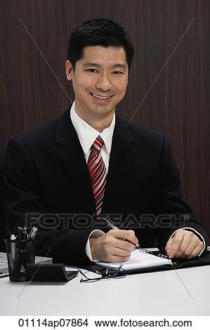 A businessman in a suit sits at his desk View Large Photo Image Picture - A businessman in a suit sits at his desk. Fotosearch