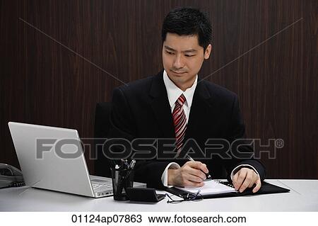 A businessman in a suit sits at his desk View Large Photo Image Stock Image - A businessman in a suit sits at his desk. Fotosearch