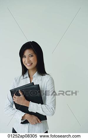 A businesswoman looks at the camera as she holds a folder View Large Photo Image Stock Photography - A businesswoman looks at the camera as she holds a folder. Fotosearch
