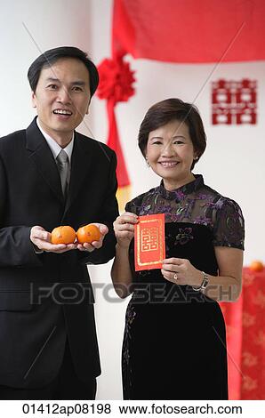 A couple look at the camera as they hold two oranges and a red envelope View Large Photo Image Stock Photo - A couple look at the camera as they hold two oranges and a red envelope. Fotosearch