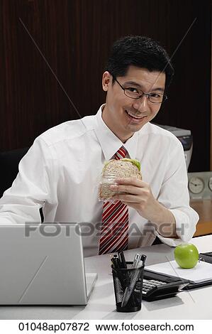 A man eats lunch at his desk View Large Photo Image Stock Image - A man eats lunch at his desk. Fotosearch