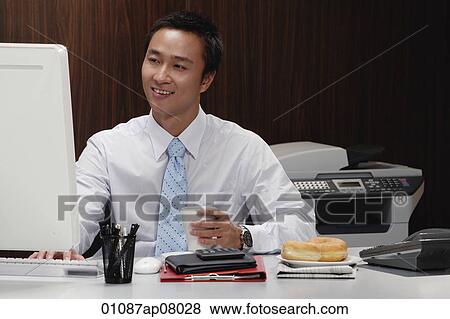 A man has a hot drink while he works at his desk View Large Photo Image Stock Photo - A man has a hot drink while he works at his desk. Fotosearch