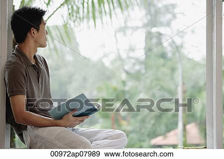 A man holds a book as he looks out a window View Large Photo Image Stock Photo - A man holds a book as he looks out a window. Fotosearch