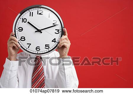 A man holds a clock in front of his face View Large Photo Image Stock Photo - A man holds a clock in front of his face. Fotosearch