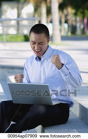 A man is excited as he uses his laptop outdoors View Large Photo Image Stock Photo - A man is excited as he uses his laptop outdoors. Fotosearch